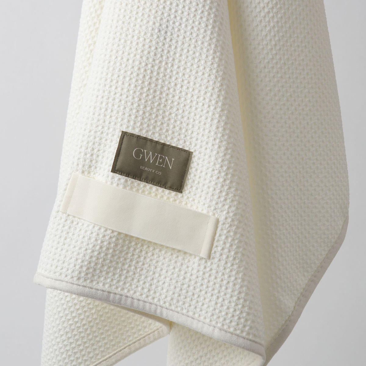 The GWEN Hair Towel in Linen, folded and hanging with the woven GWEN Beauty Co. label visible.