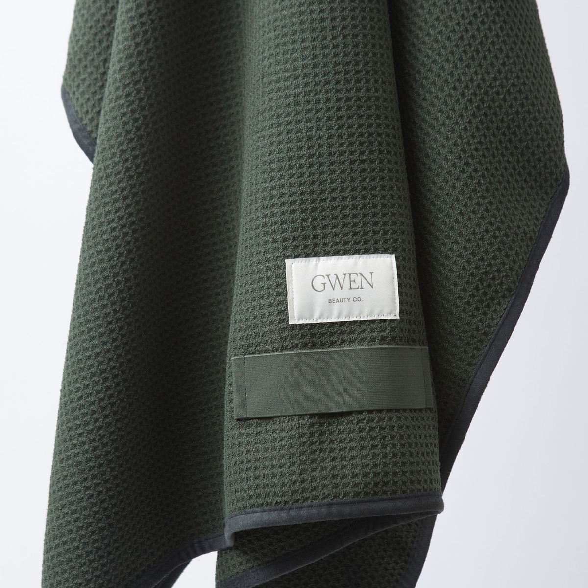 The GWEN Hair Towel in Moss, the limited-edition colorway, folded and hanging with the woven GWEN Beauty Co. label visible.