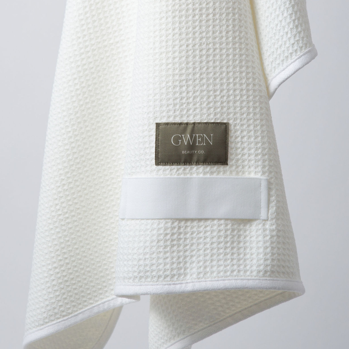 The GWEN Hair Towel in Ivory, folded and hanging with the woven GWEN Beauty Co. label visible.