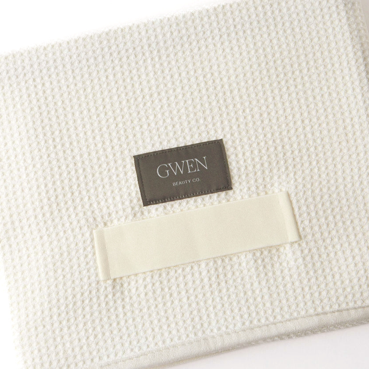 The GWEN Hair Towel in Linen laid flat at an angle, showing the waffle weave texture and the GWEN Beauty Co. label.