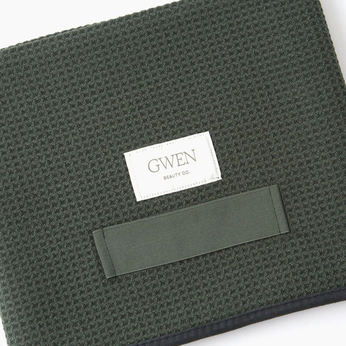 The GWEN Hair Towel in Moss laid flat at an angle, showing the waffle weave texture and the GWEN Beauty Co. label.