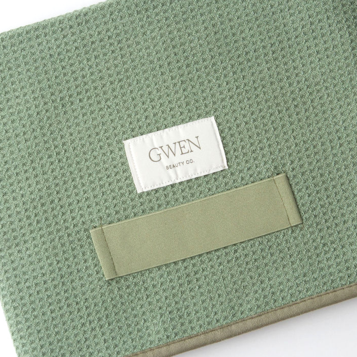 The GWEN Hair Towel in Sage laid flat at an angle, showing the waffle weave texture and the GWEN Beauty Co. label.