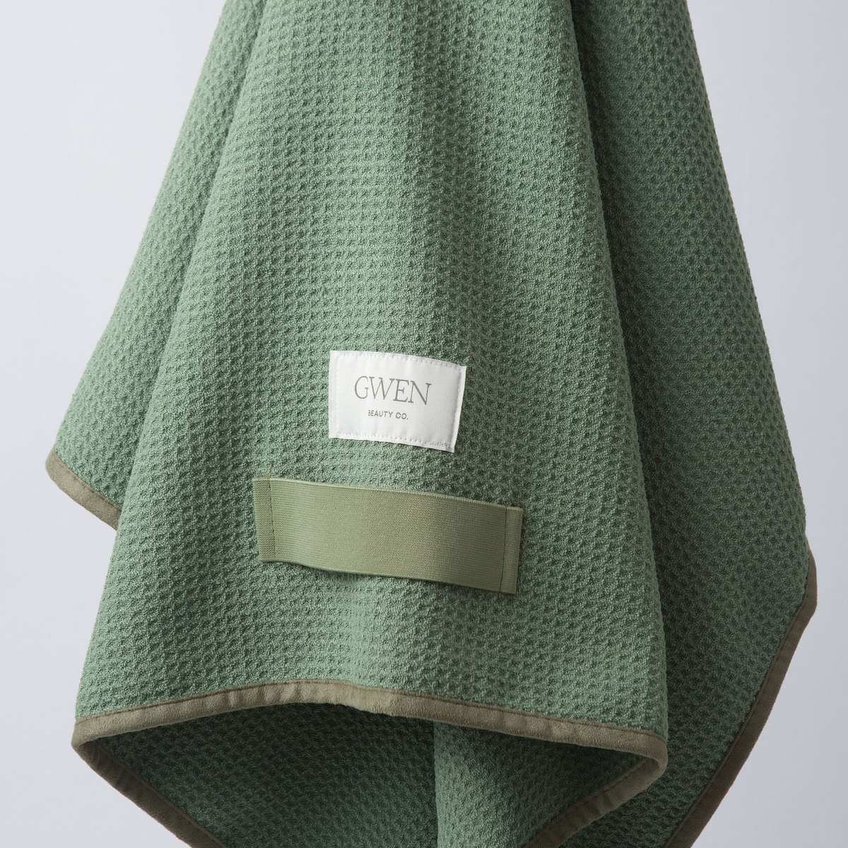 The GWEN Hair Towel in Sage, folded and hanging with the woven GWEN Beauty Co. label visible.