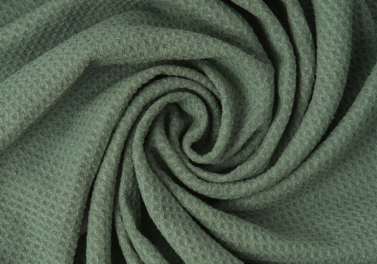 A close-up of textured sage green GWEN hair towel arranged in a spiral swirl, showing the woven material detail.